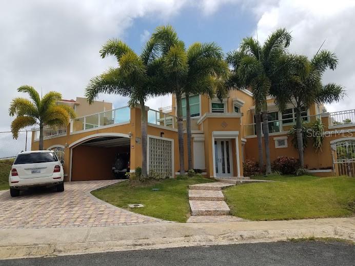 A two-story yellow house with a covered carport, palm trees, and a paved driveway — The Village at the Hill MANGO BEACH CORNER UNIT 116, CEIBA, PR