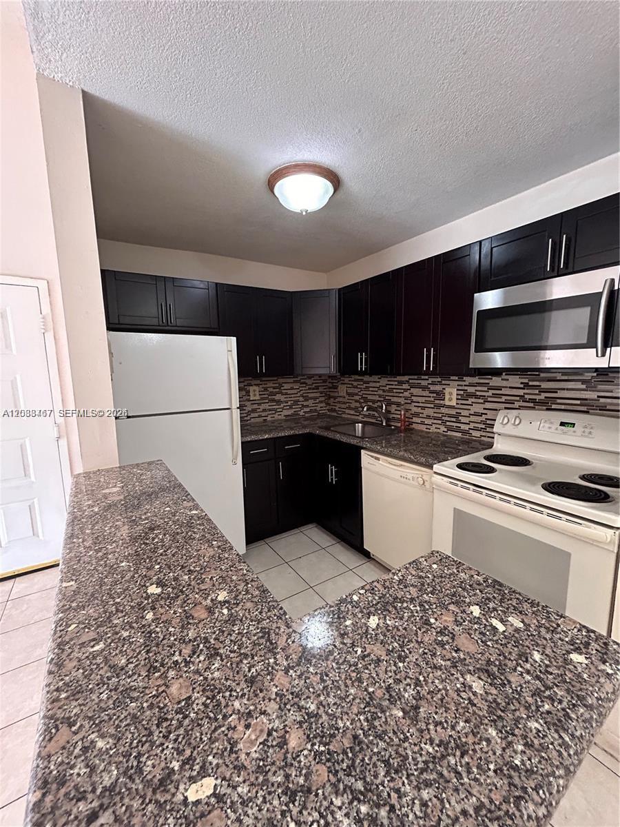 A kitchen features dark wood cabinets, granite countertops, and white appliances — 15630 SW 80th St # 305, Miami FL 33193, MIAMI, FL