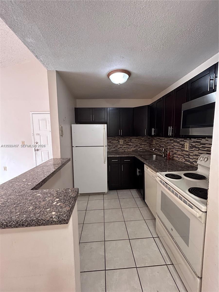 A kitchen features dark wood cabinets, granite countertops, white appliances, and light-colored floor tiles — 15630 SW 80th St # 305, Miami FL 33193, MIAMI, FL