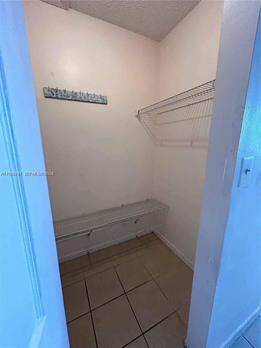 A small walk-in closet features white wire shelving, a wall-mounted coat rack, and tiled flooring — 15630 SW 80th St # 305, Miami FL 33193, MIAMI, FL