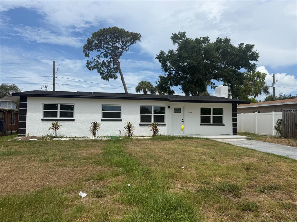 A single-story white house with a black roof and trim sits behind a grassy yard — 4910 HALIFAX DRIVE, TAMPA, FL