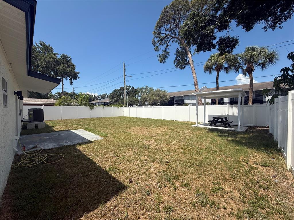 A fenced backyard features a concrete patio, a small covered pergola, and a picnic table — 4910 HALIFAX DRIVE, TAMPA, FL