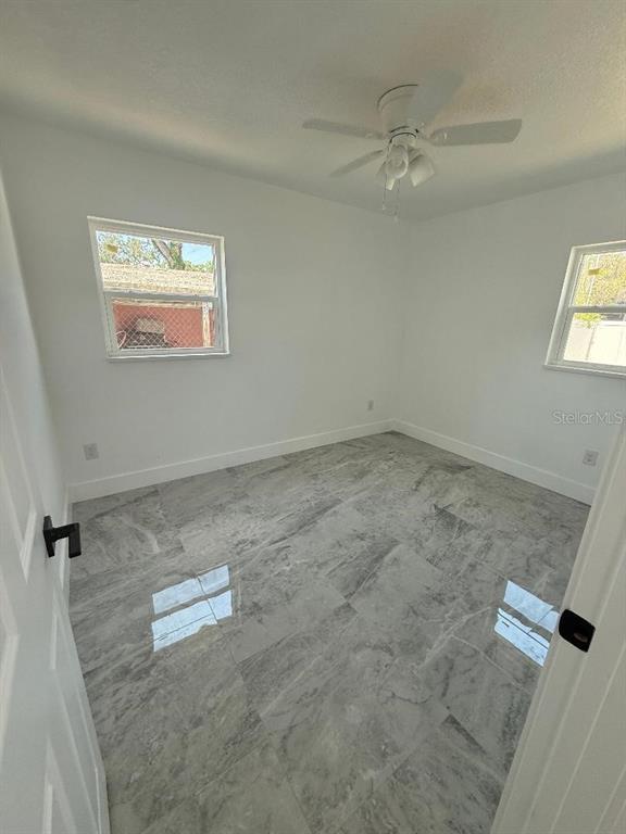 A bedroom with white walls, a ceiling fan, and gray marble-look tile flooring — 4910 HALIFAX DRIVE, TAMPA, FL
