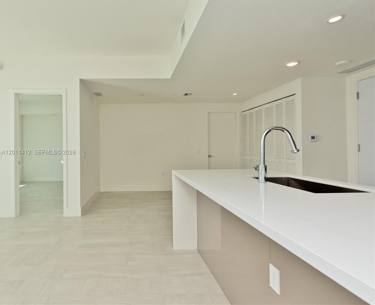 A modern kitchen features a white quartz island with a sink and light-colored flooring — 2000 Metropica Way # 2206, Sunrise FL 33323, SUNRISE, FL