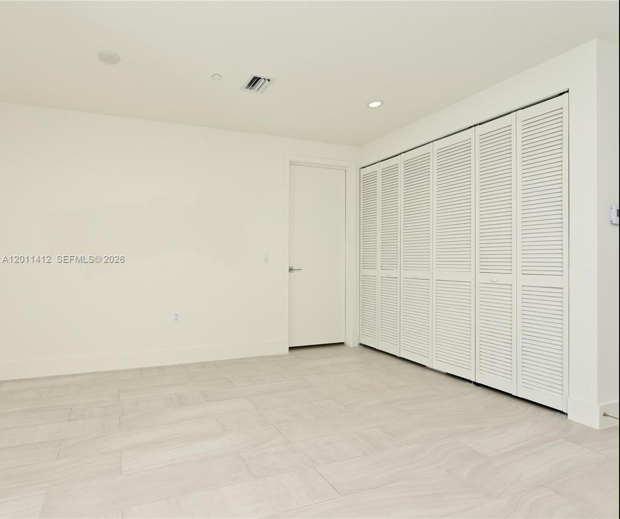 An empty room features white walls, light-colored tile flooring, a closet with louvered doors, and a door — 2000 Metropica Way # 2206, Sunrise FL 33323, SUNRISE, FL
