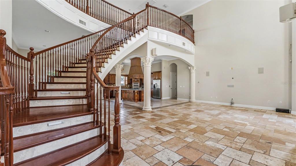 A grand foyer features a curved wooden staircase, stone tile flooring, and arched architectural columns — 1282 MCGEE ROAD, PLANT CITY, FL
