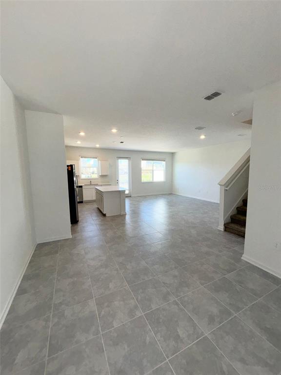 An open-concept living area features light gray tile flooring, a kitchen island, and a staircase — 164 BOGEY DRIVE, DAVENPORT, FL