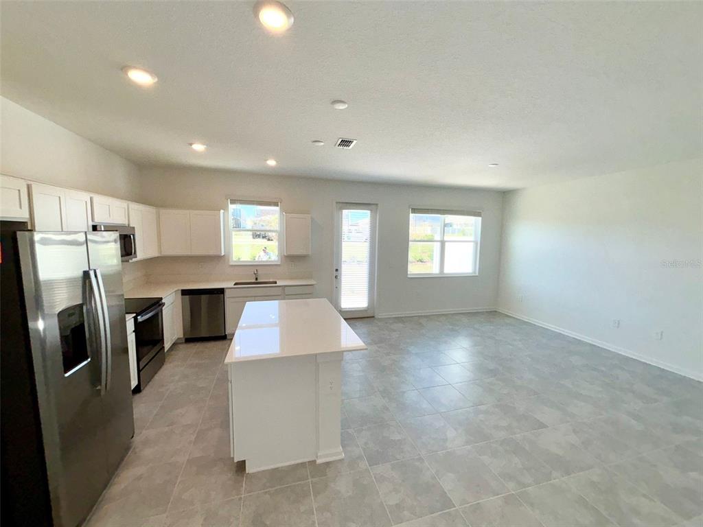 A kitchen with white cabinets, stainless steel appliances, and a central island opens to a living area — 164 BOGEY DRIVE, DAVENPORT, FL