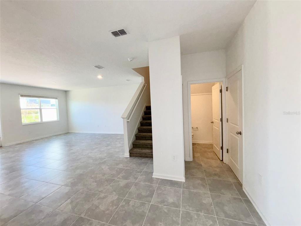 An open living area features light gray tile flooring, a carpeted staircase, and a doorway — 164 BOGEY DRIVE, DAVENPORT, FL