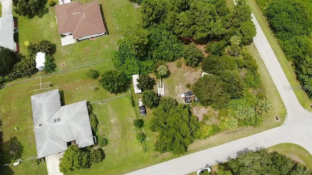 An aerial view shows a residential lot with trees, a driveway, and nearby houses — 21360 WICKER AVENUE, PORT CHARLOTTE, FL