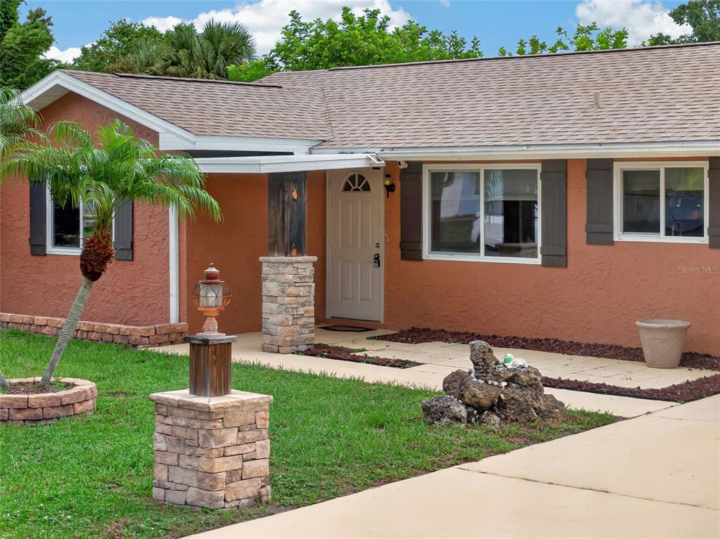 A single-story house with a terracotta-colored exterior, stone-accented pillars, and a paved walkway — 7582 LYNCREST STREET, NORTH PORT, FL