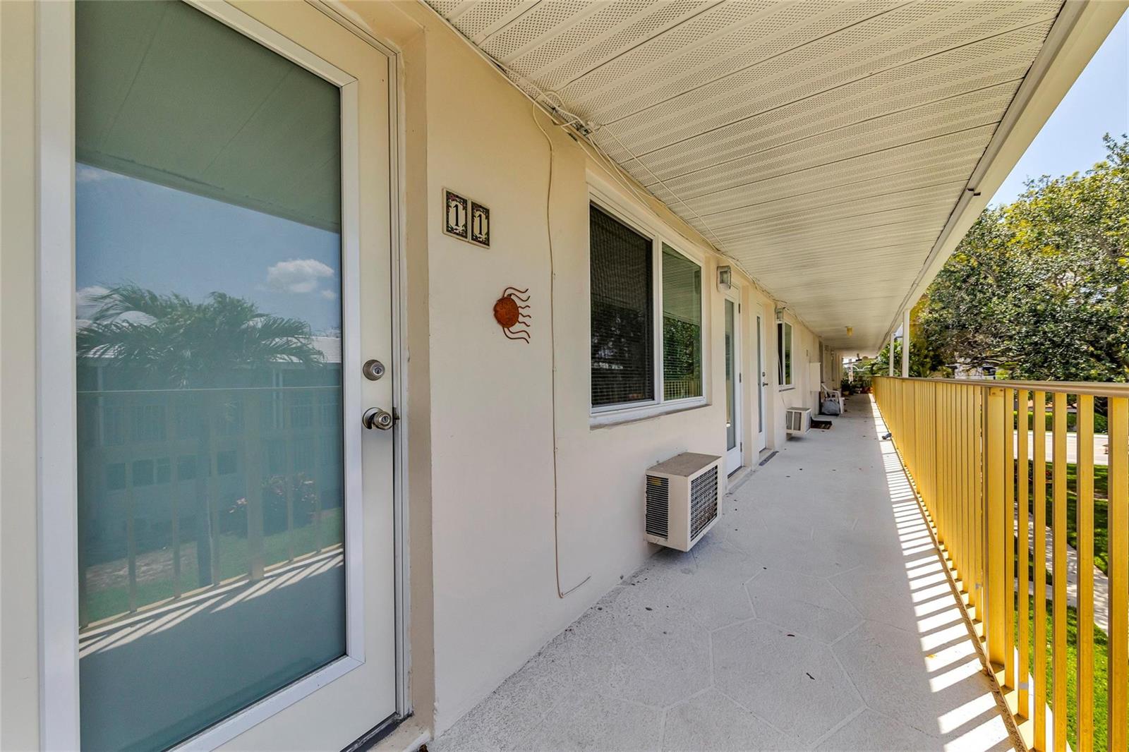 An exterior walkway with a yellow railing, a white door, and a window air conditioner — 11 SW 4th Avenue # 11, Boca Raton FL 33432, BOCA RATON, FL