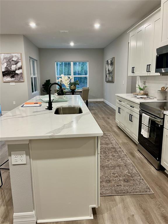 A modern kitchen features white cabinetry, a marble-topped island with a sink, and wood flooring — 11272 GALLINULE AVENUE, BROOKSVILLE, FL