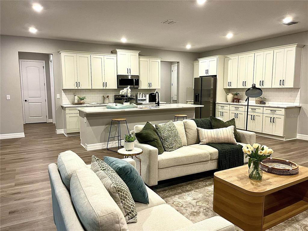 An open-concept kitchen and living area features white cabinetry, a central island, and neutral furniture — 11272 GALLINULE AVENUE, BROOKSVILLE, FL