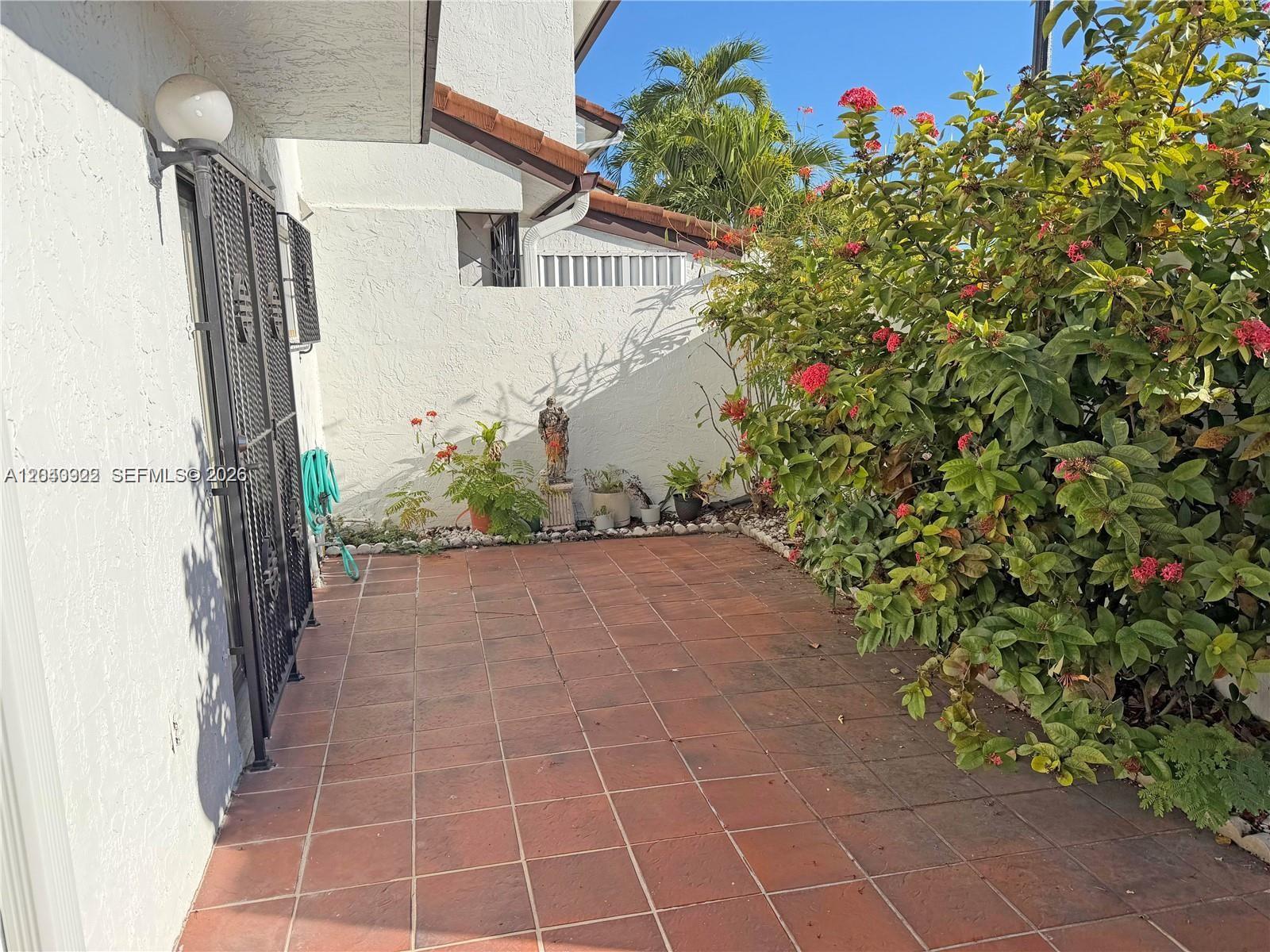 A tiled patio area features a metal gate, a small statue, and flowering bushes — 1331 SW 124th Ct # 3, Miami FL 33184, MIAMI, FL