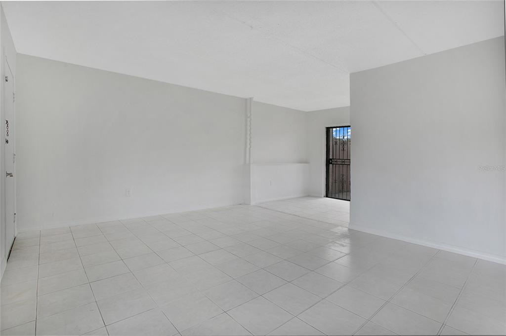 An empty room features white tiled floors, plain walls, and a door with a security gate — 1914 HONOUR ROAD UNIT 2, ORLANDO, FL