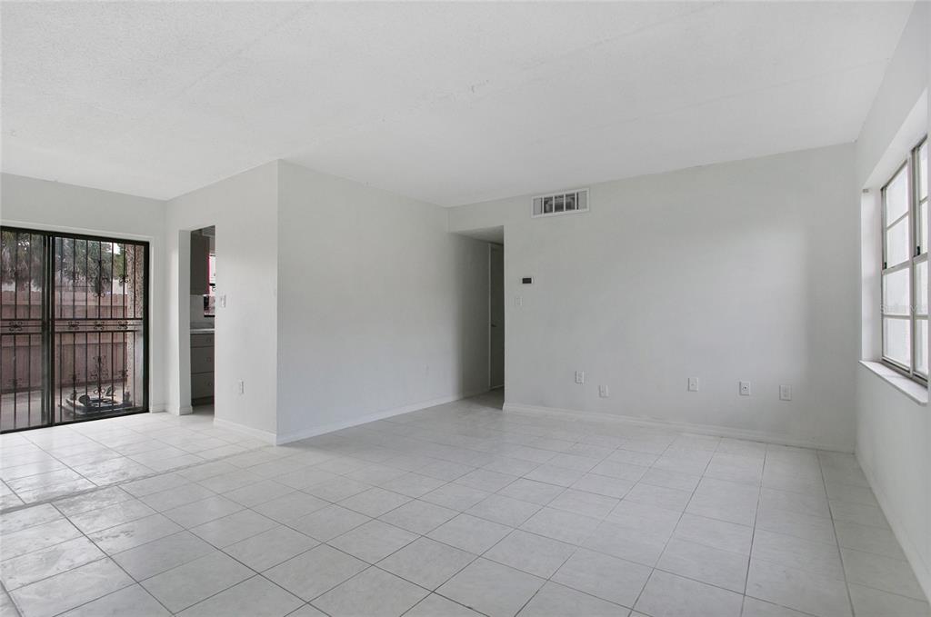 An empty living room features white tile flooring, white walls, and a sliding glass door — 1914 HONOUR ROAD UNIT 2, ORLANDO, FL