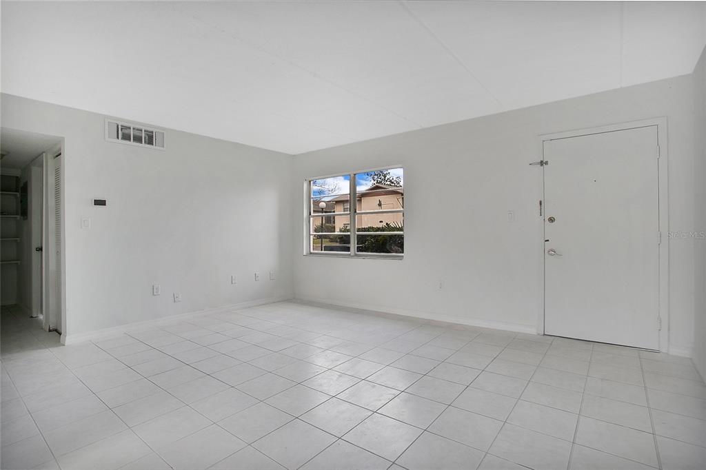 An empty room features white tiled floors, light gray walls, a window, and a white door — 1914 HONOUR ROAD UNIT 2, ORLANDO, FL