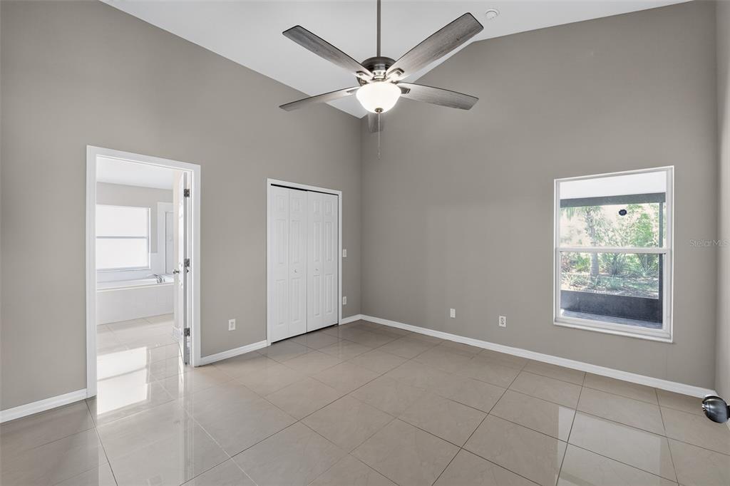 A bedroom with gray walls, tile flooring, a ceiling fan, and an attached bathroom — 4027 LONGWORTH LOOP, KISSIMMEE, FL