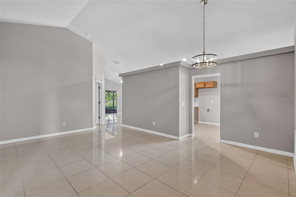 A spacious room with light-colored tile flooring, gray walls, and a modern chandelier — 4027 LONGWORTH LOOP, KISSIMMEE, FL