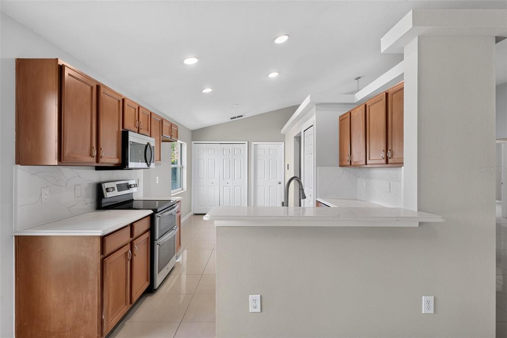 A kitchen features wood cabinets, white countertops, stainless steel appliances, and light-colored tile flooring — 4027 LONGWORTH LOOP, KISSIMMEE, FL