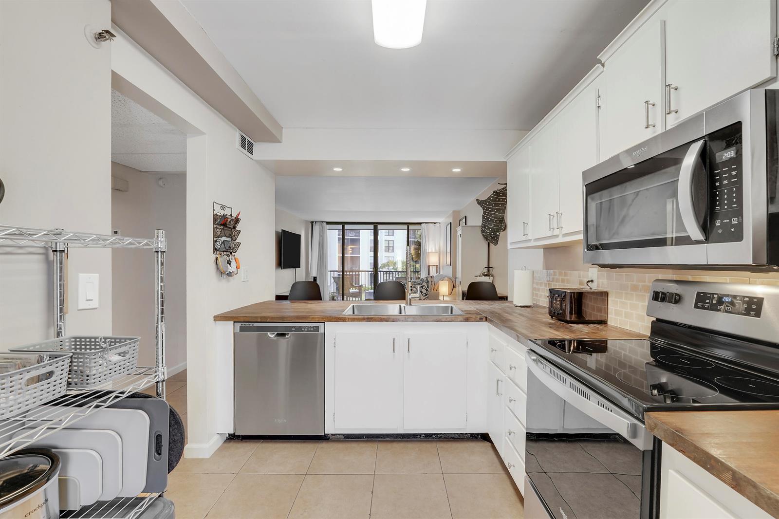 A kitchen with white cabinets, stainless steel appliances, and a wood countertop overlooks a living area — 20 Royal Palm Way # 204, Boca Raton FL 33432, BOCA RATON, FL