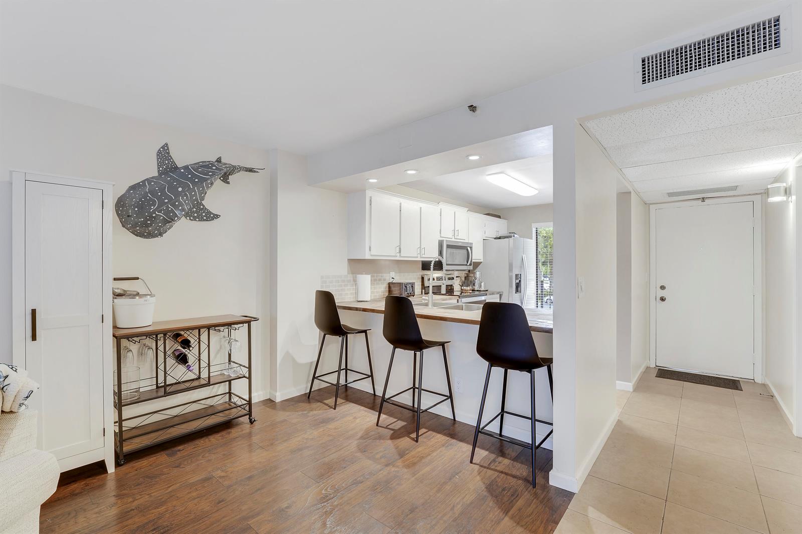 A kitchen with white cabinets and a breakfast bar overlooks a dining area with a bar cart — 20 Royal Palm Way # 204, Boca Raton FL 33432, BOCA RATON, FL