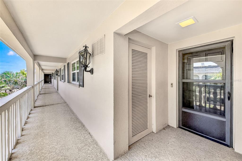 An outdoor apartment hallway features a white railing, a louvered utility door, and a screen door — 147 BLUFF VIEW DRIVE UNIT 304, LARGO, FL