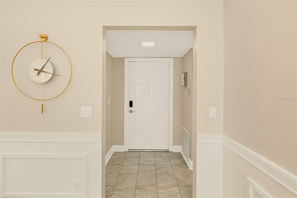An entryway features a white door, tiled floor, and a large gold wall clock — 147 BLUFF VIEW DRIVE UNIT 304, LARGO, FL