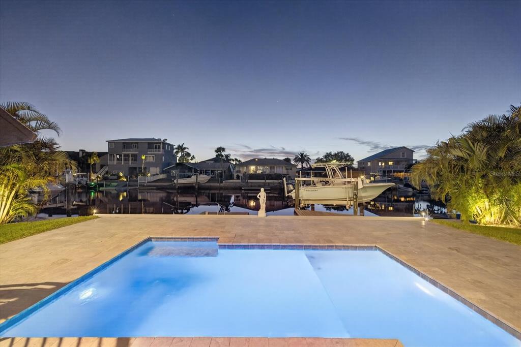 A swimming pool sits on a patio overlooking a canal with docked boats at dusk — 5101 SOUTH SHORE DRIVE, NEW PORT RICHEY, FL
