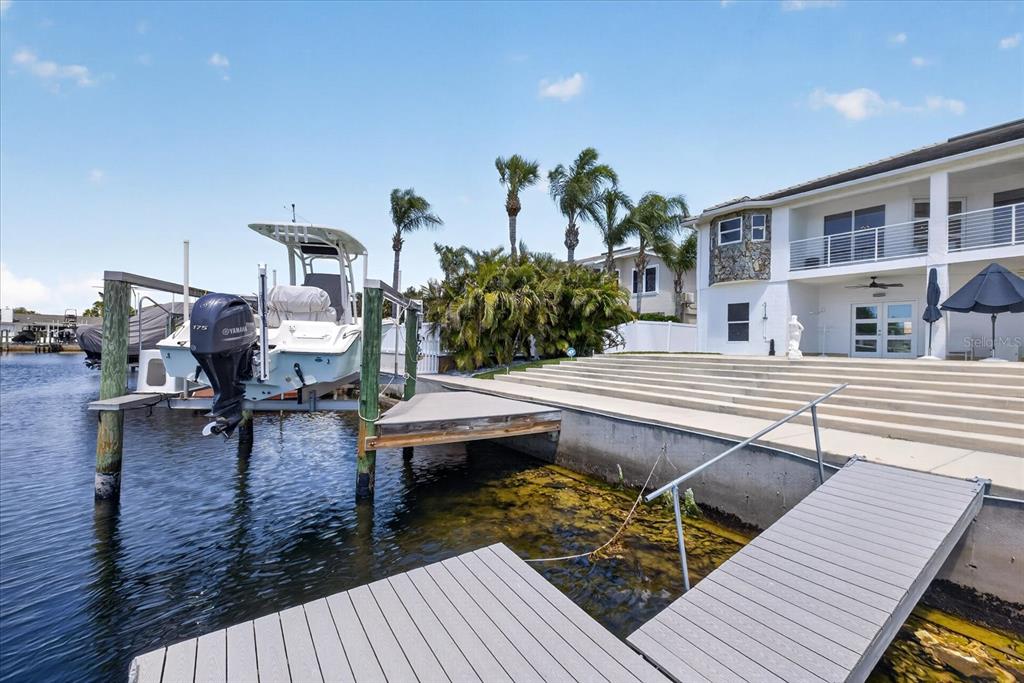 A waterfront backyard features a boat lift, a dock, and concrete steps leading to a house — 5101 SOUTH SHORE DRIVE, NEW PORT RICHEY, FL