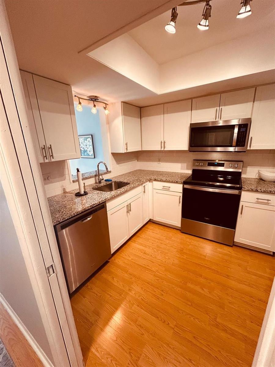A kitchen features white cabinets, granite countertops, stainless steel appliances, and light wood flooring — 2050 Oleander Boulevard # 703, Fort Pierce FL 34950, FORT PIERCE, FL