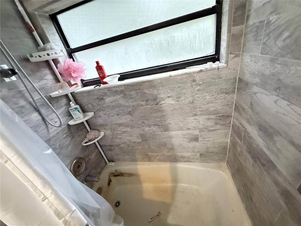 A bathtub with a shower head and a multi-tiered corner shelf against gray tiled walls — 1521 W SAINT ELIZABETH PLACE, CITRUS SPRINGS, FL
