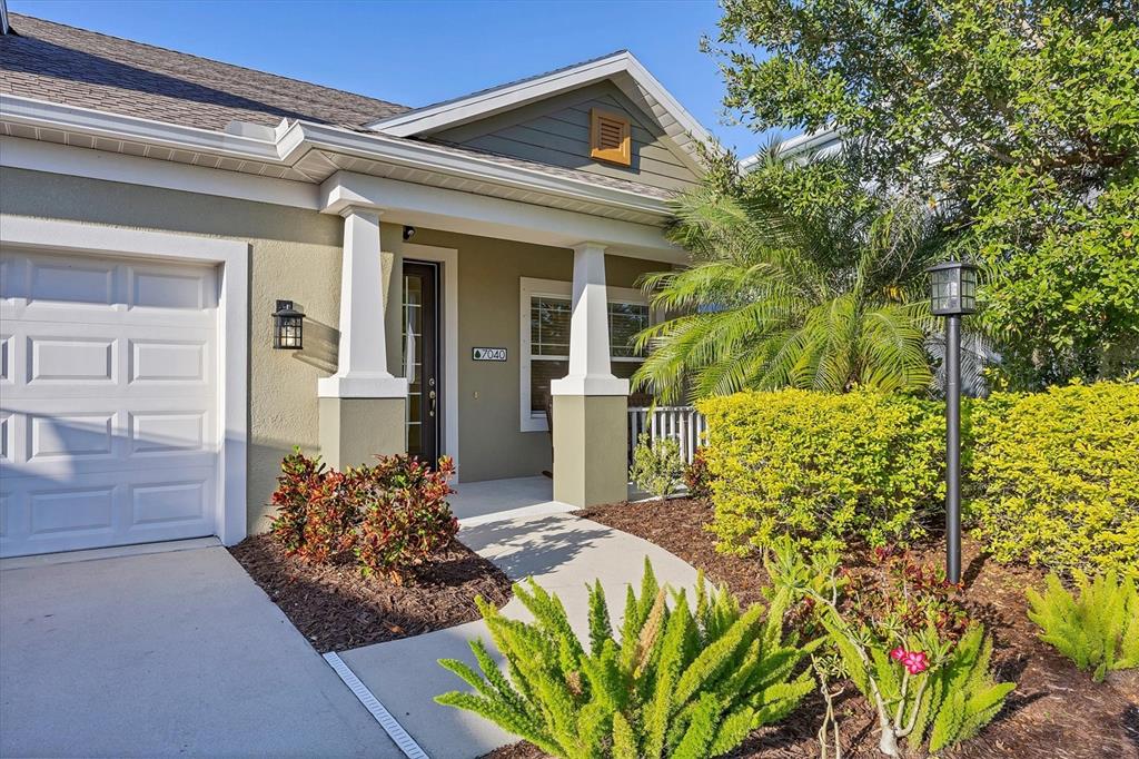 The exterior of a single-story house features a garage, a covered porch, and landscaping — 7040 WHITE WILLOW COURT, SARASOTA, FL