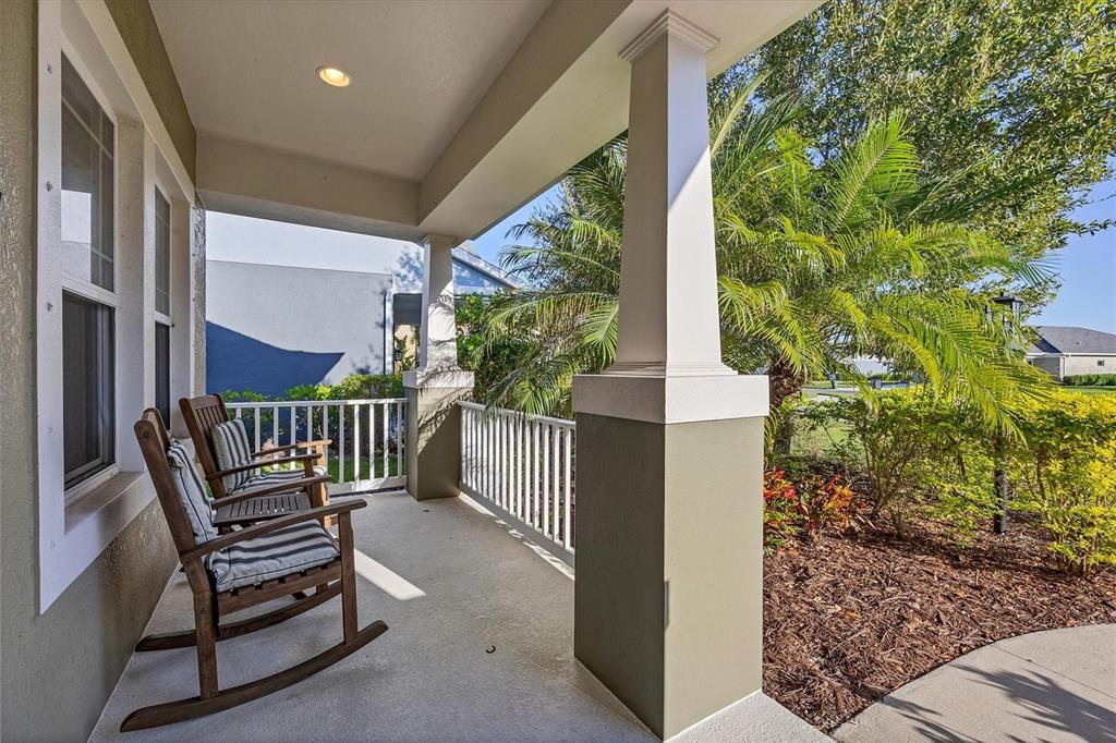 A covered front porch features two wooden rocking chairs, white railings, and square support columns — 7040 WHITE WILLOW COURT, SARASOTA, FL