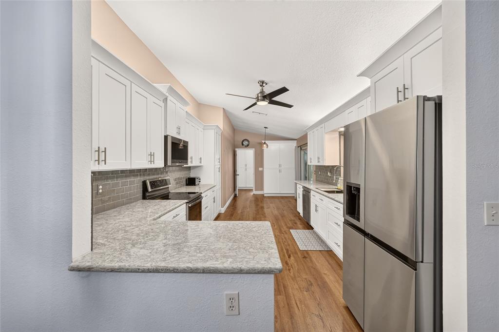 A kitchen features white cabinetry, granite countertops, stainless steel appliances, and wood-look flooring — 14845 SW 112TH CIRCLE, DUNNELLON, FL