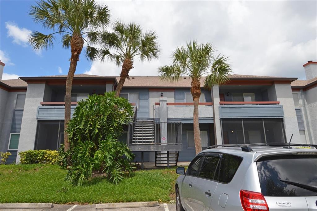 A two-story apartment building exterior with palm trees, a central staircase, and a parked car — 10265 GANDY BOULEVARD N UNIT 1002, ST PETERSBURG, FL