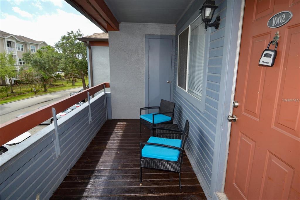 An outdoor balcony features two chairs with blue cushions and a red entry door — 10265 GANDY BOULEVARD N UNIT 1002, ST PETERSBURG, FL