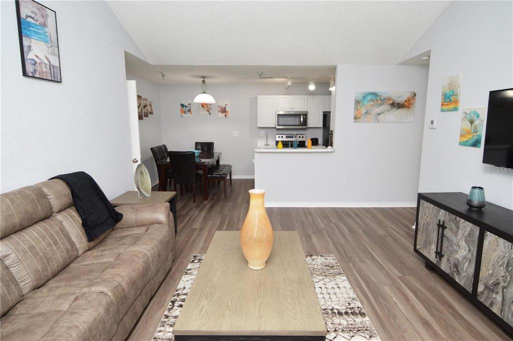 A living room with wood-look flooring, a brown sofa, and an open kitchen beyond — 10265 GANDY BOULEVARD N UNIT 1002, ST PETERSBURG, FL