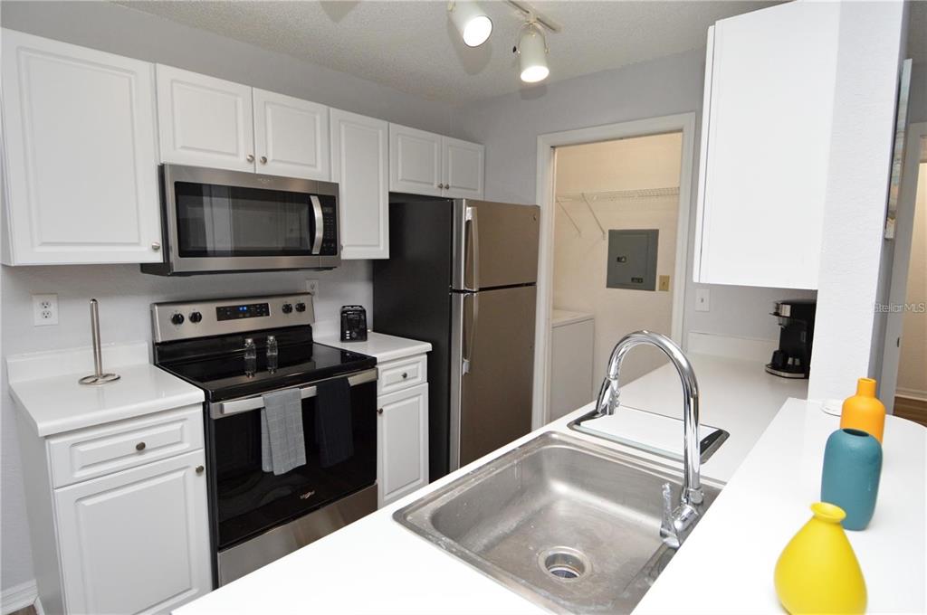 A kitchen features white cabinets, stainless steel appliances, a sink, and a pantry doorway — 10265 GANDY BOULEVARD N UNIT 1002, ST PETERSBURG, FL