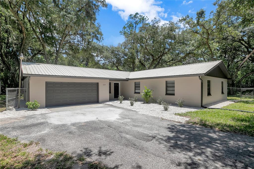 A single-story house with a metal roof, beige brick exterior, and an attached garage — 1609 ITCHEPACKESASSA DRIVE, LAKELAND, FL