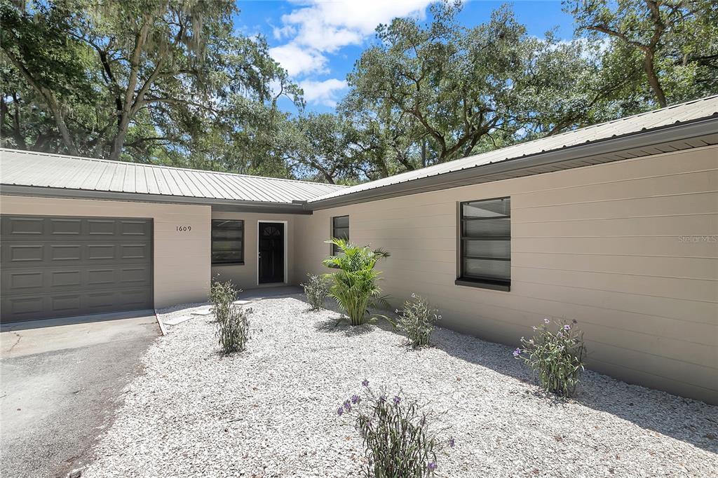 A single-story house with a beige exterior, metal roof, and a gravel front yard — 1609 ITCHEPACKESASSA DRIVE, LAKELAND, FL