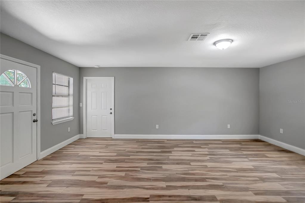 An empty room features gray walls, wood-look flooring, two white doors, and a window — 1609 ITCHEPACKESASSA DRIVE, LAKELAND, FL