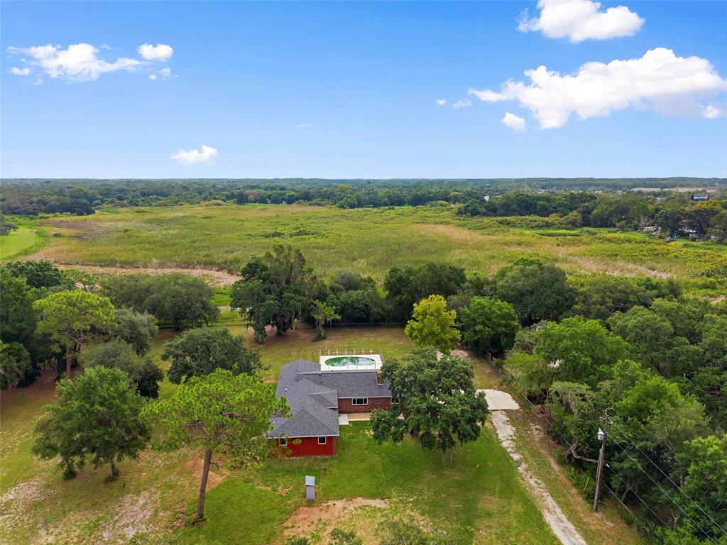 An aerial view shows a red brick house with a pool and large backyard — 10115 FRIERSON LAKE DRIVE, HUDSON, FL