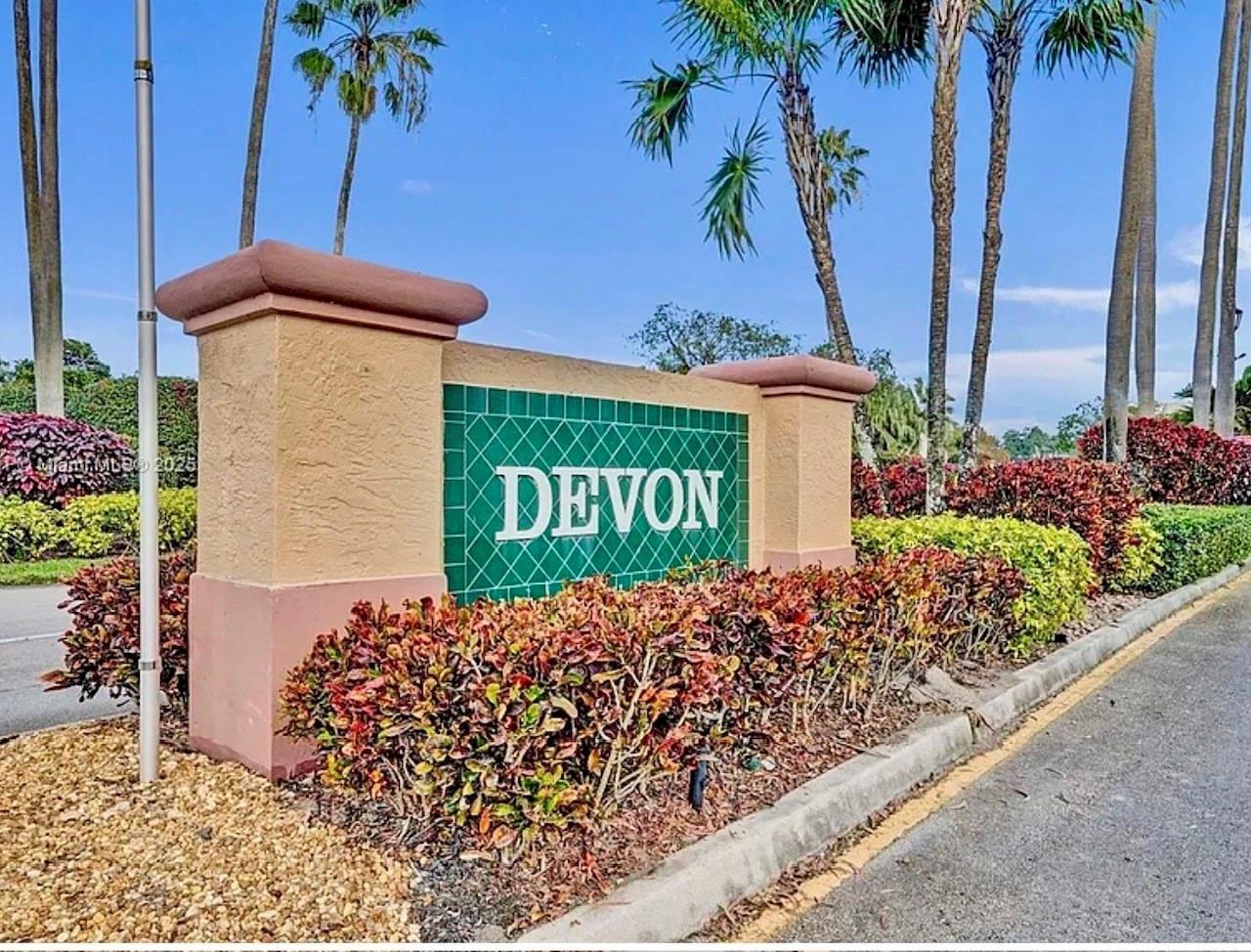A tan stucco monument sign with the word "DEVON" sits beside a road with landscaping — 7302 S Devon Drive # 307, Tamarac FL 33321, TAMARAC, FL