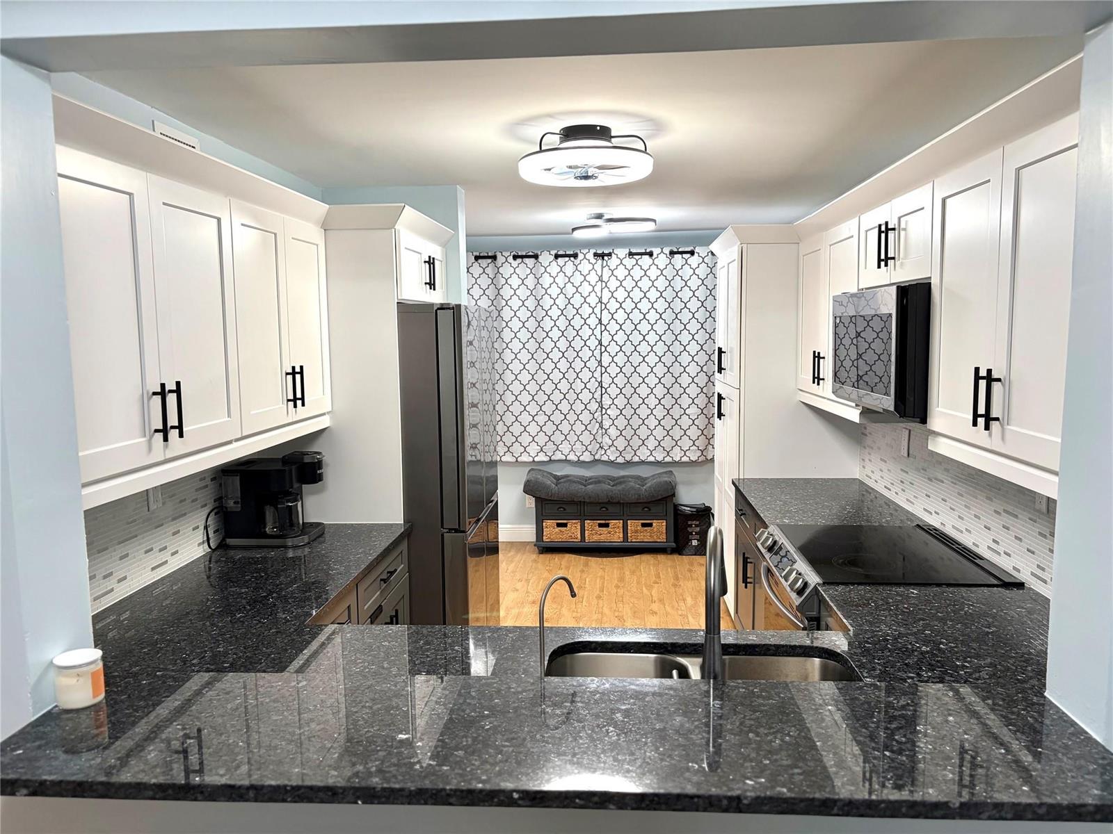 A galley-style kitchen features white cabinets, dark granite countertops, and stainless steel appliances — 7302 S Devon Drive # 307, Tamarac FL 33321, TAMARAC, FL