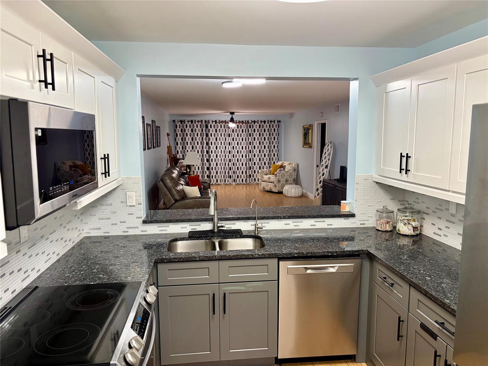 A kitchen with gray lower cabinets, white upper cabinets, dark countertops, and a pass-through window — 7302 S Devon Drive # 307, Tamarac FL 33321, TAMARAC, FL