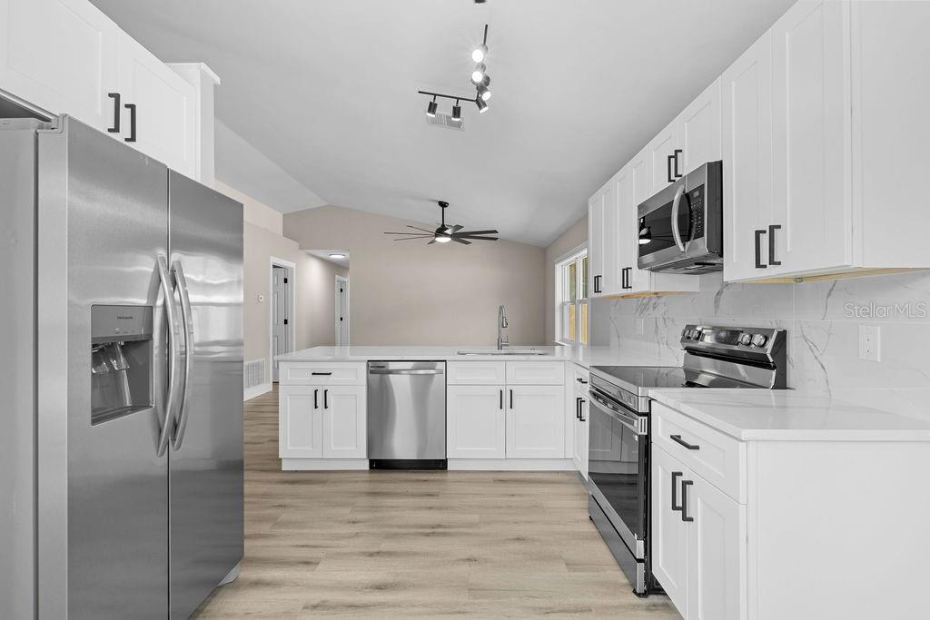 A modern kitchen features white cabinets, stainless steel appliances, and light wood-look flooring — 6330 RUTHIE DRIVE, ORLANDO, FL