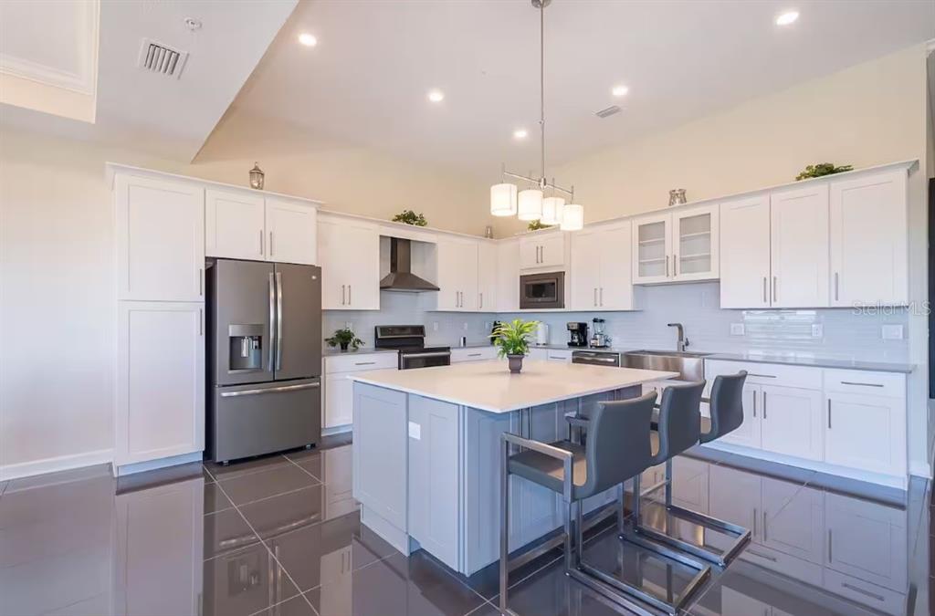 A modern kitchen features white cabinetry, a gray island with seating, and stainless steel appliances — 4731 CLOCK TOWER DRIVE UNIT 401, KISSIMMEE, FL