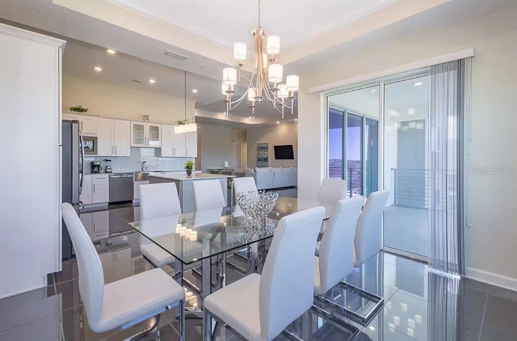 A dining area with a glass table and white chairs sits adjacent to a modern kitchen — 4731 CLOCK TOWER DRIVE UNIT 401, KISSIMMEE, FL